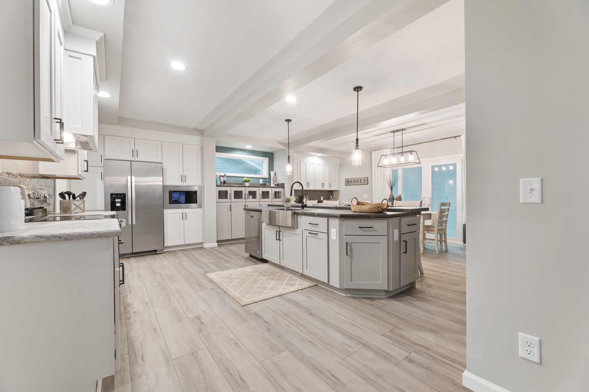 Modern kitchen with open layout, featuring a central island with pendant lights, stainless steel appliances, white cabinets, and light wood flooring.