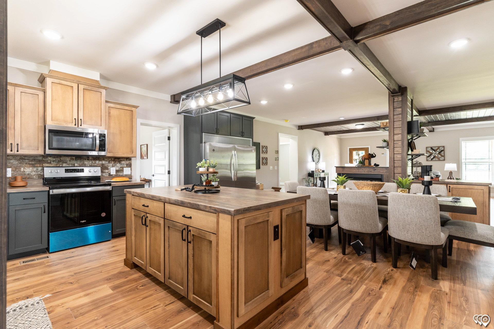 Modern farmhouse kitchen and dining area with wooden floors. Features light wood cabinets, central island, stainless steel appliances, and rustic decor.