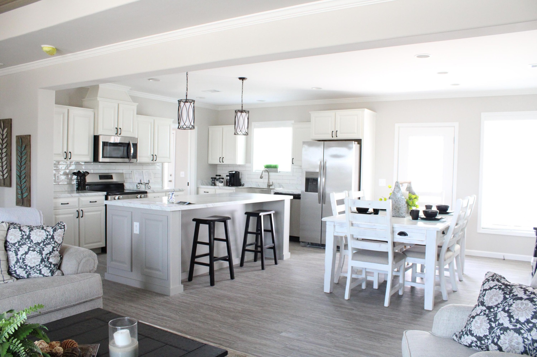 Bright, modern kitchen with white cabinets, stainless steel appliances, and a center island with stools. Cozy dining area with a white table and chairs. Airy and inviting.