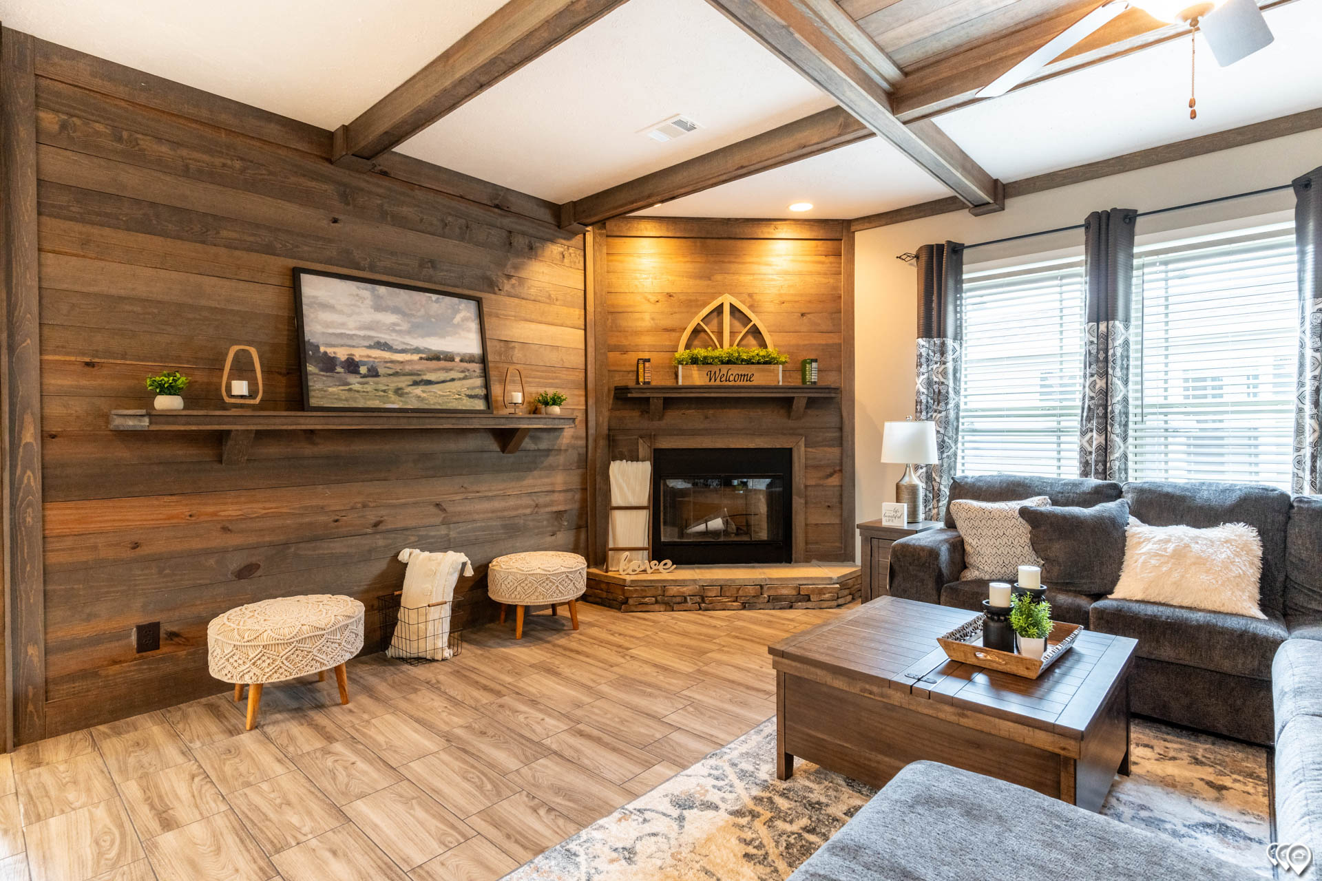 Cozy living room with wood paneling, a stone fireplace, and rustic decor. Soft gray couches, a wooden coffee table, and plush accents create a warm ambiance.