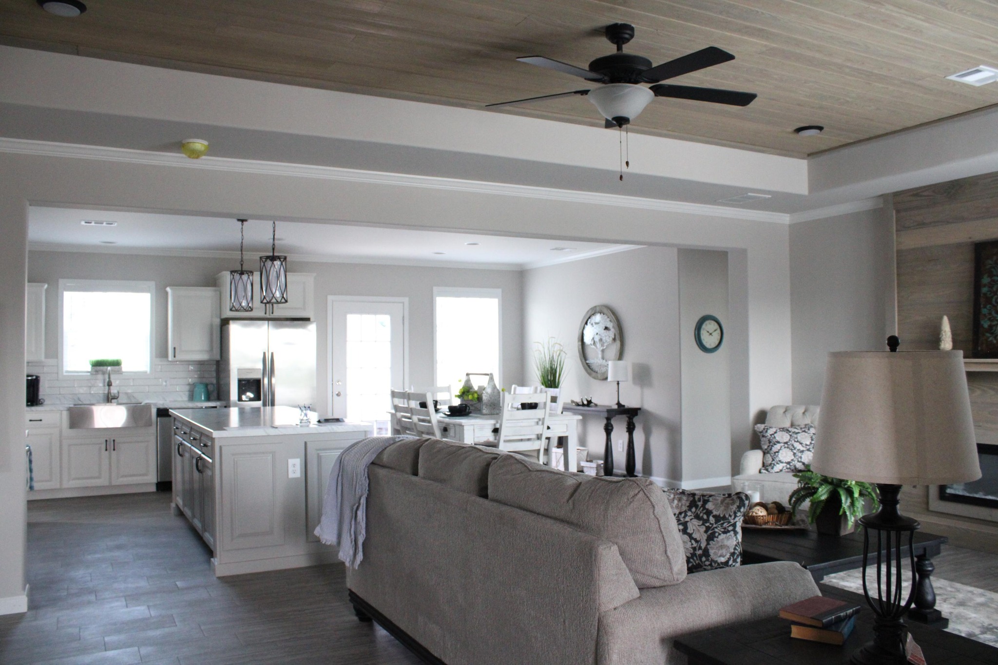 Spacious open-concept living area with grey tones; features a kitchen, dining area, and cozy seating. Ceiling fan and soft lighting create a calm ambiance.