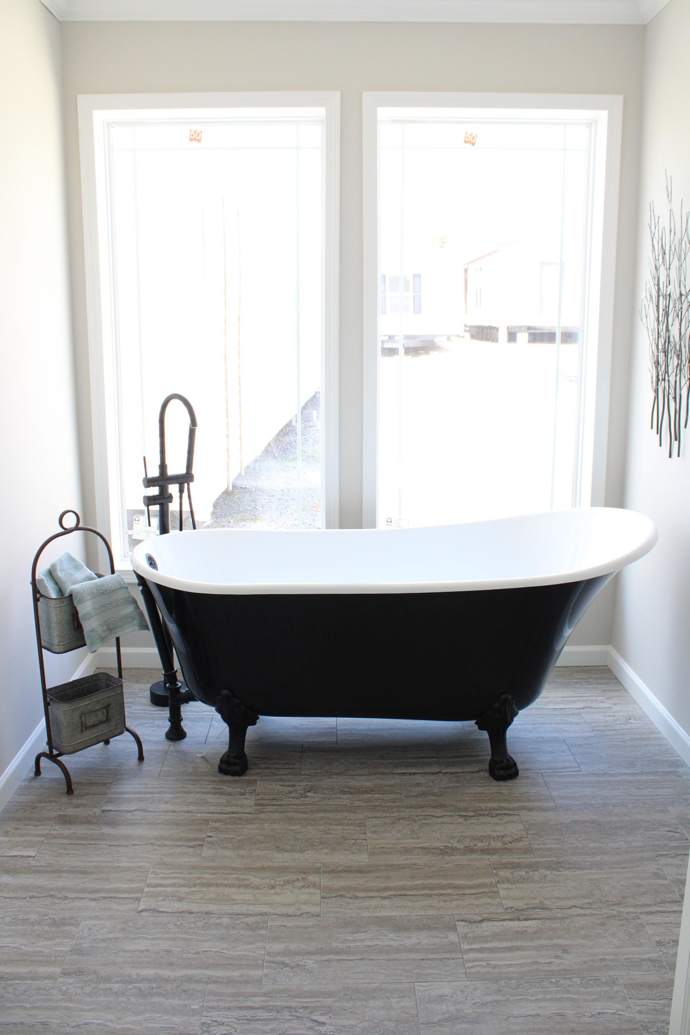 Elegant bathroom with a black clawfoot tub set against large bright windows. A towel rack holds folded towels, creating a serene and minimalist vibe.