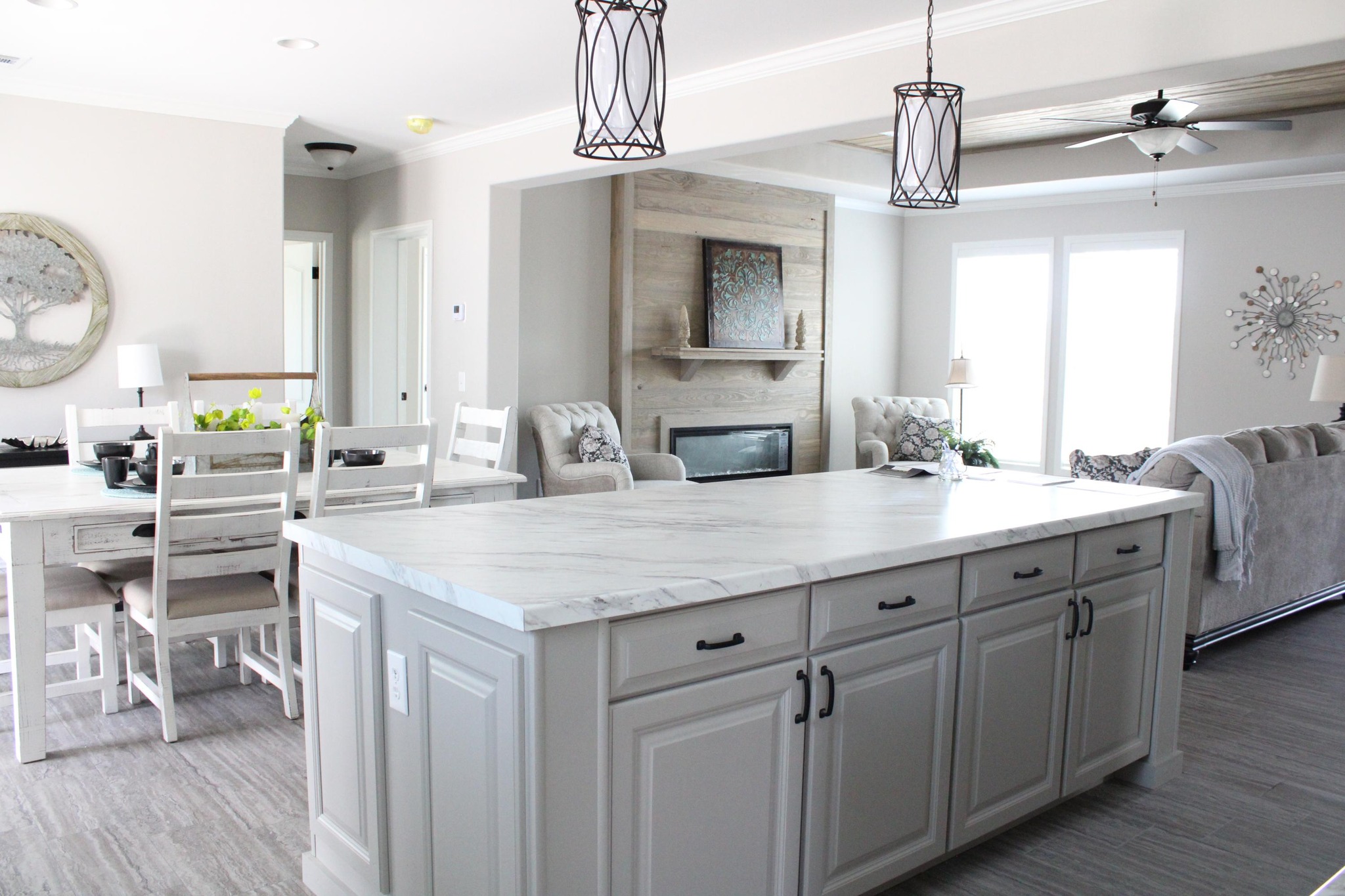 Spacious kitchen and living area with a marble island, white cabinetry, cozy dining table, modern pendant lights, and a warm seating area by the fireplace.