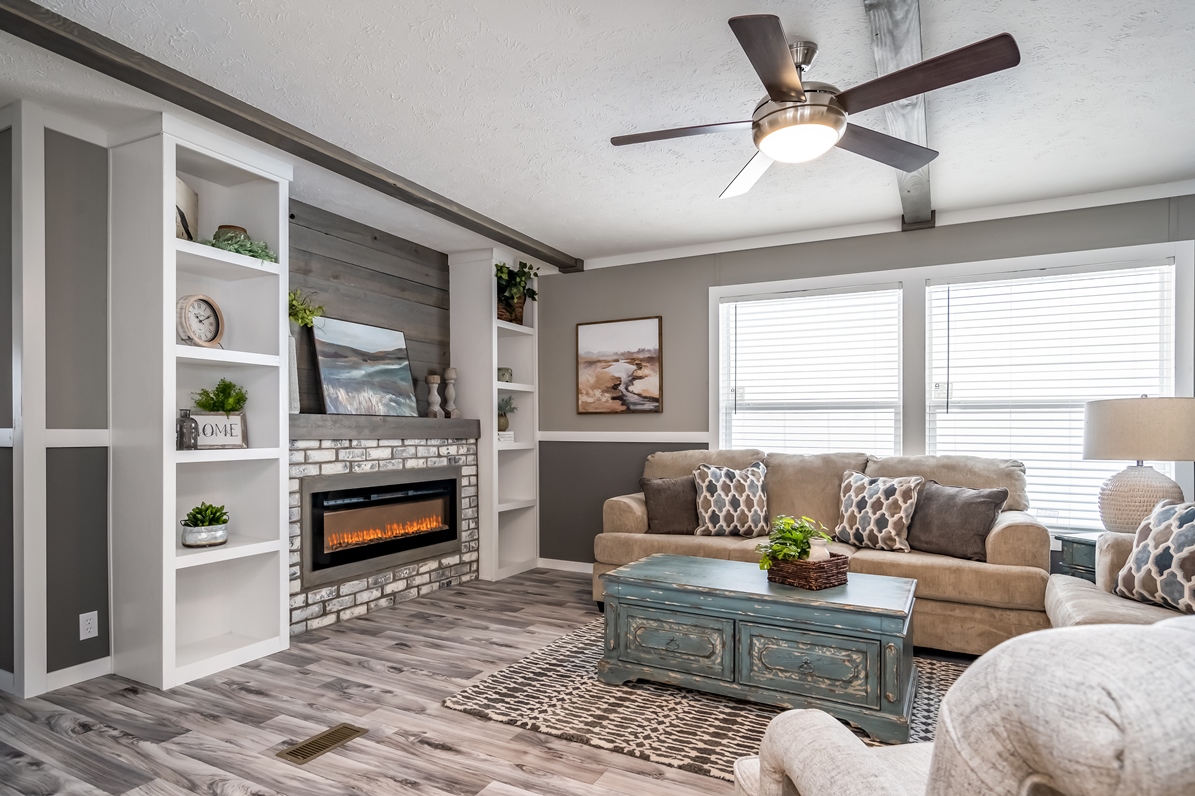 Cozy living room with a modern, rustic vibe. Features a beige sofa, patterned cushions, stone fireplace, and teal coffee table. Bright, inviting atmosphere.