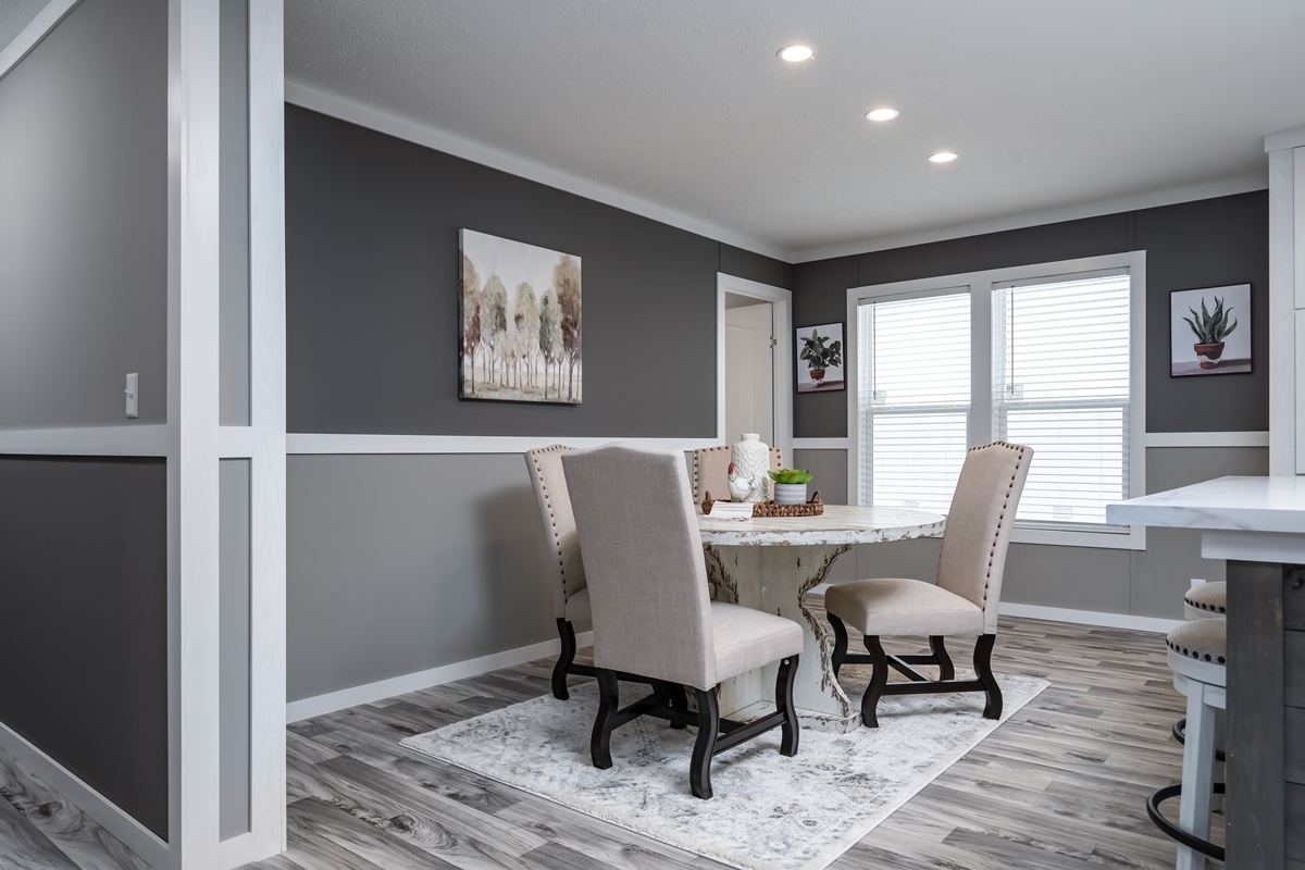 Modern dining room with a white marble table, four beige upholstered chairs on a patterned rug, gray walls, large windows, and abstract wall art.
