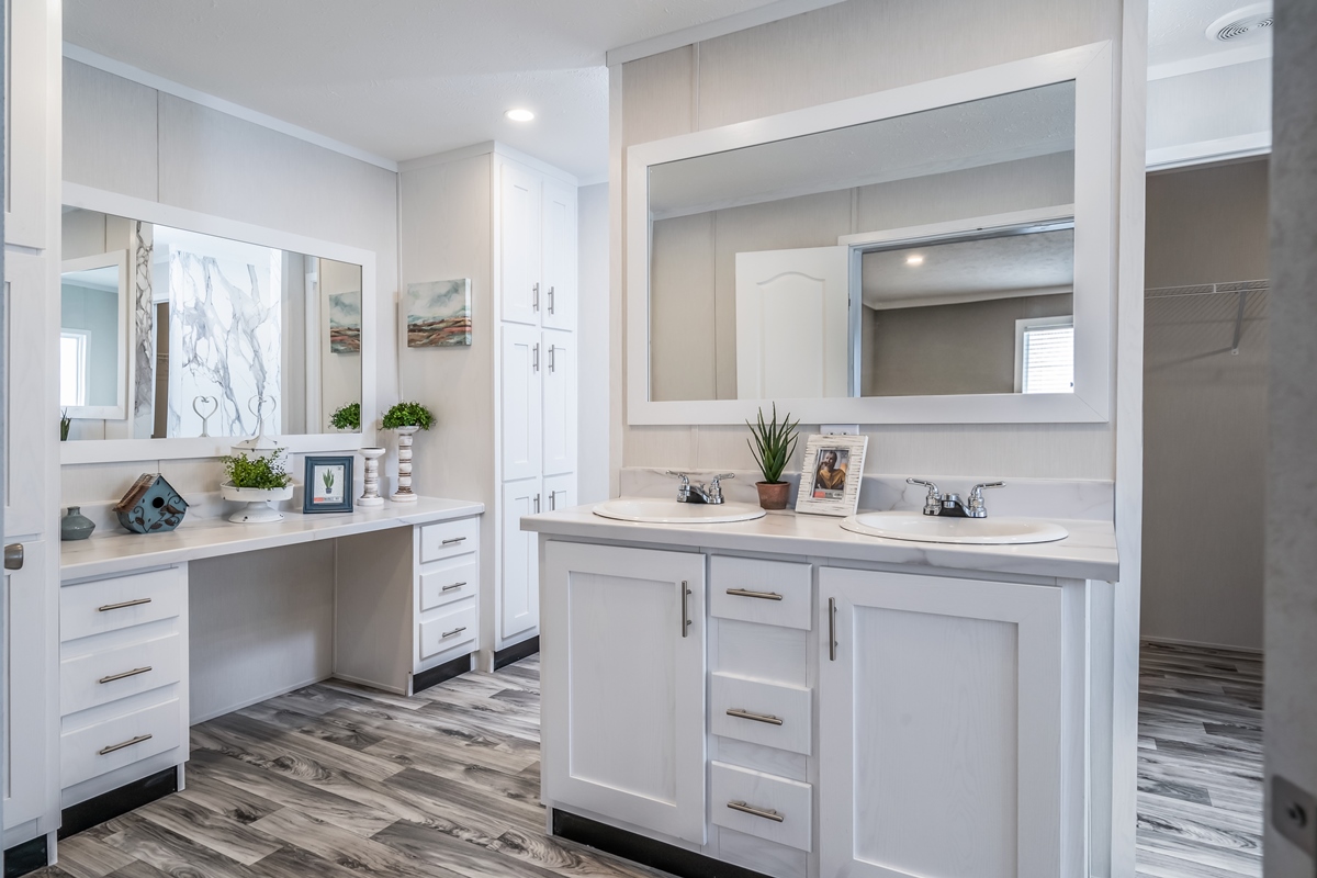 Modern bathroom with double sinks, large mirrors, white cabinetry, and elegant gray flooring. Decor includes potted plants and framed artwork.