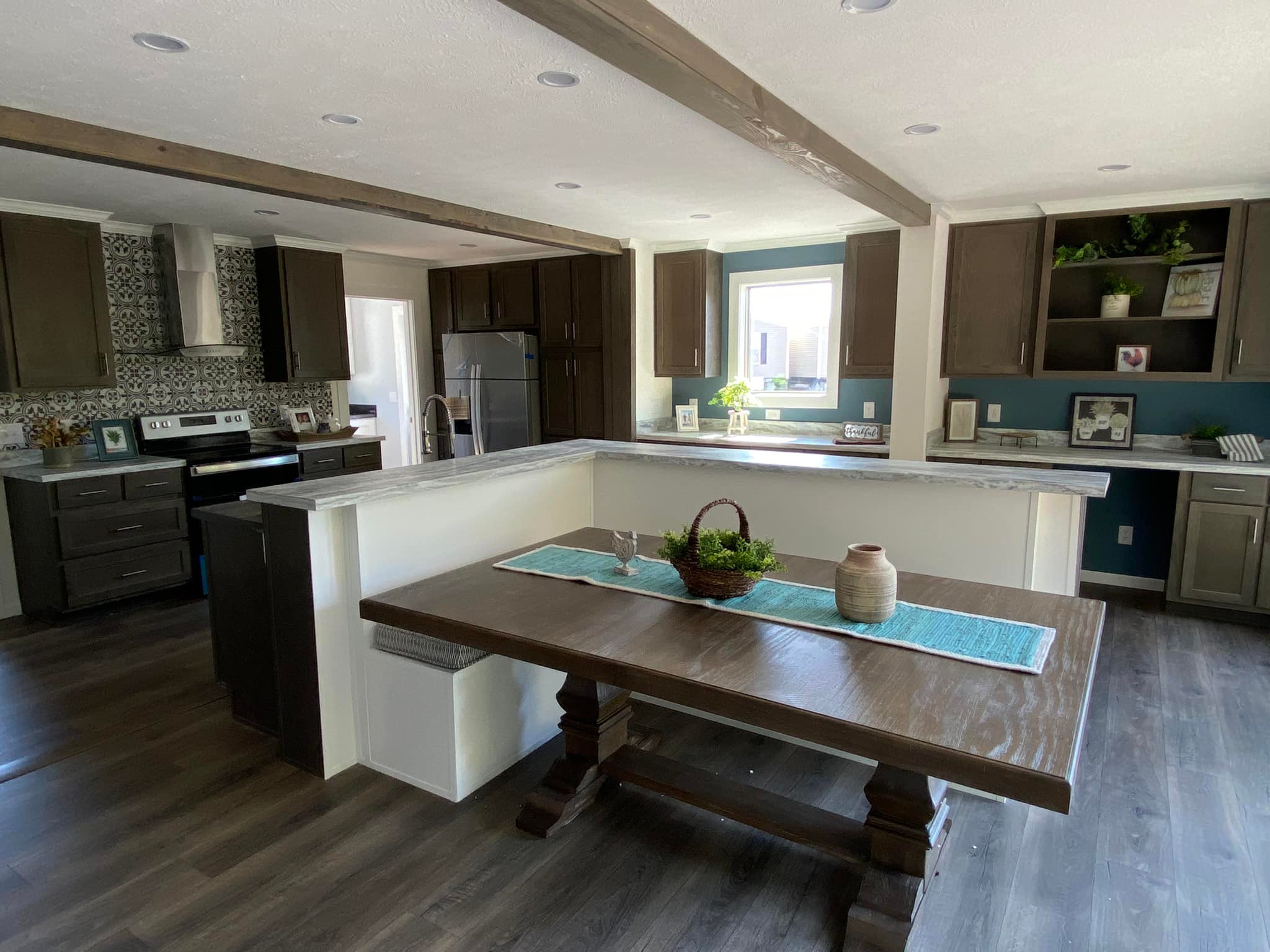 Modern kitchen with dark wood cabinets, marble countertops, and a patterned backsplash. A wooden dining table holds a basket centerpiece. Bright and inviting.