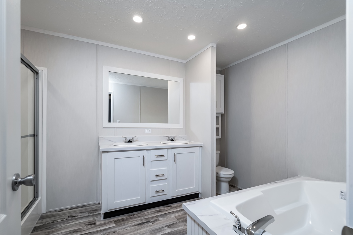Modern bathroom with a white double vanity, large mirror, recessed lighting, and a corner bathtub. Neutral tones and wood-look flooring create a serene atmosphere.