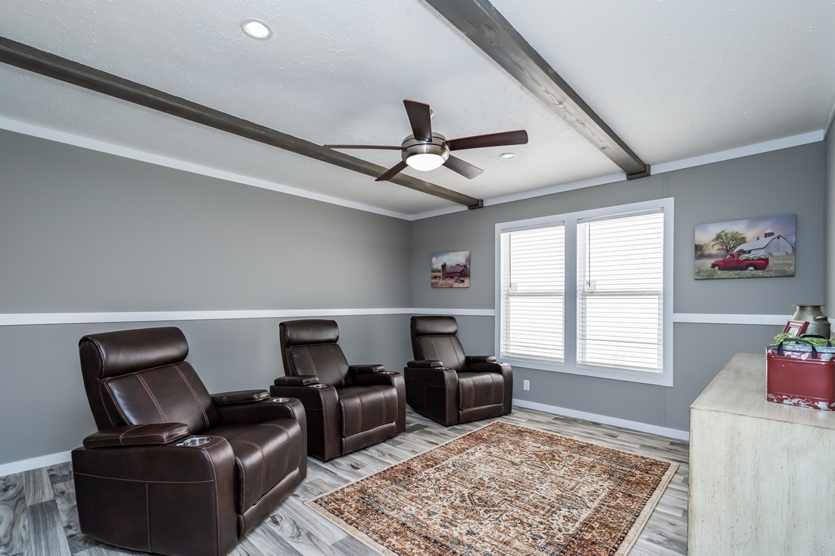 A modern home theater room features three brown leather recliners, a patterned rug on wood flooring, gray walls, and a ceiling fan, conveying comfort.