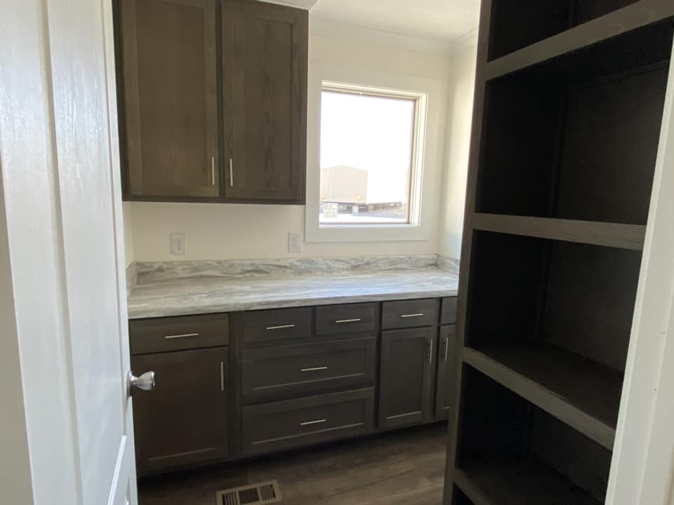 Narrow utility room with dark wood cabinets, marble countertop, and an open shelf. Sunlight streams through a window, highlighting the tidy space.