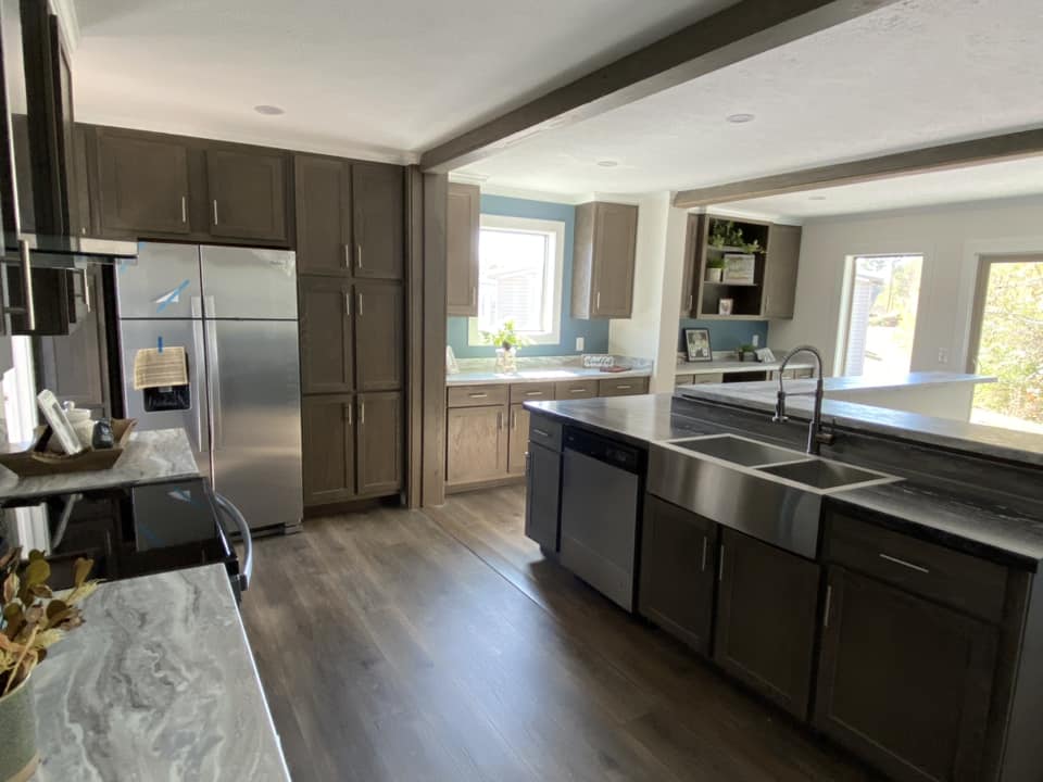 Modern kitchen with dark wood cabinets, marble countertops, and stainless steel appliances. Bright light from large windows creates a welcoming atmosphere.
