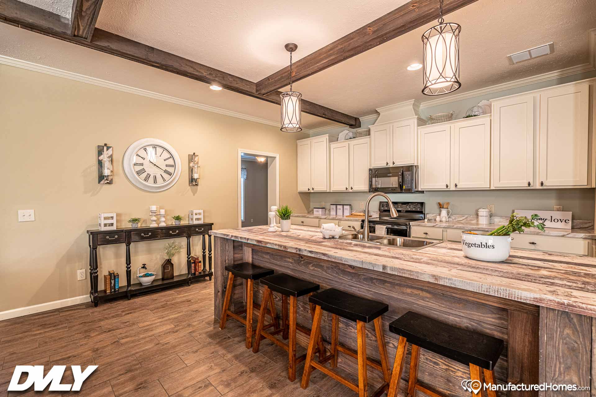Rustic kitchen with wooden beams, pendant lights, white cabinets, and a large island with a sink and four stools. Warm and inviting atmosphere.