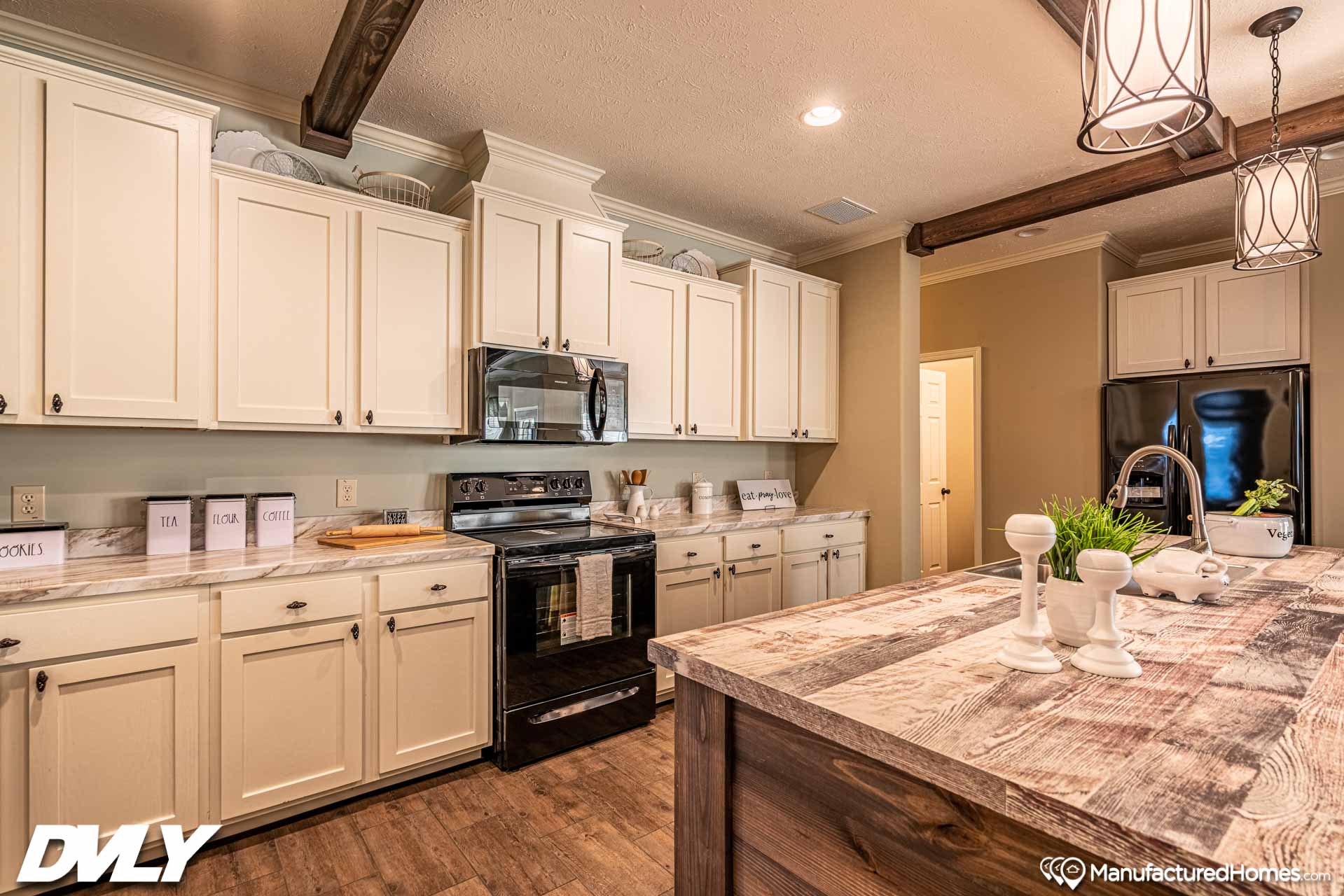 Rustic kitchen with white cabinets, dark appliances, and a wooden island. Warm lighting and modern fixtures create a cozy, inviting atmosphere.