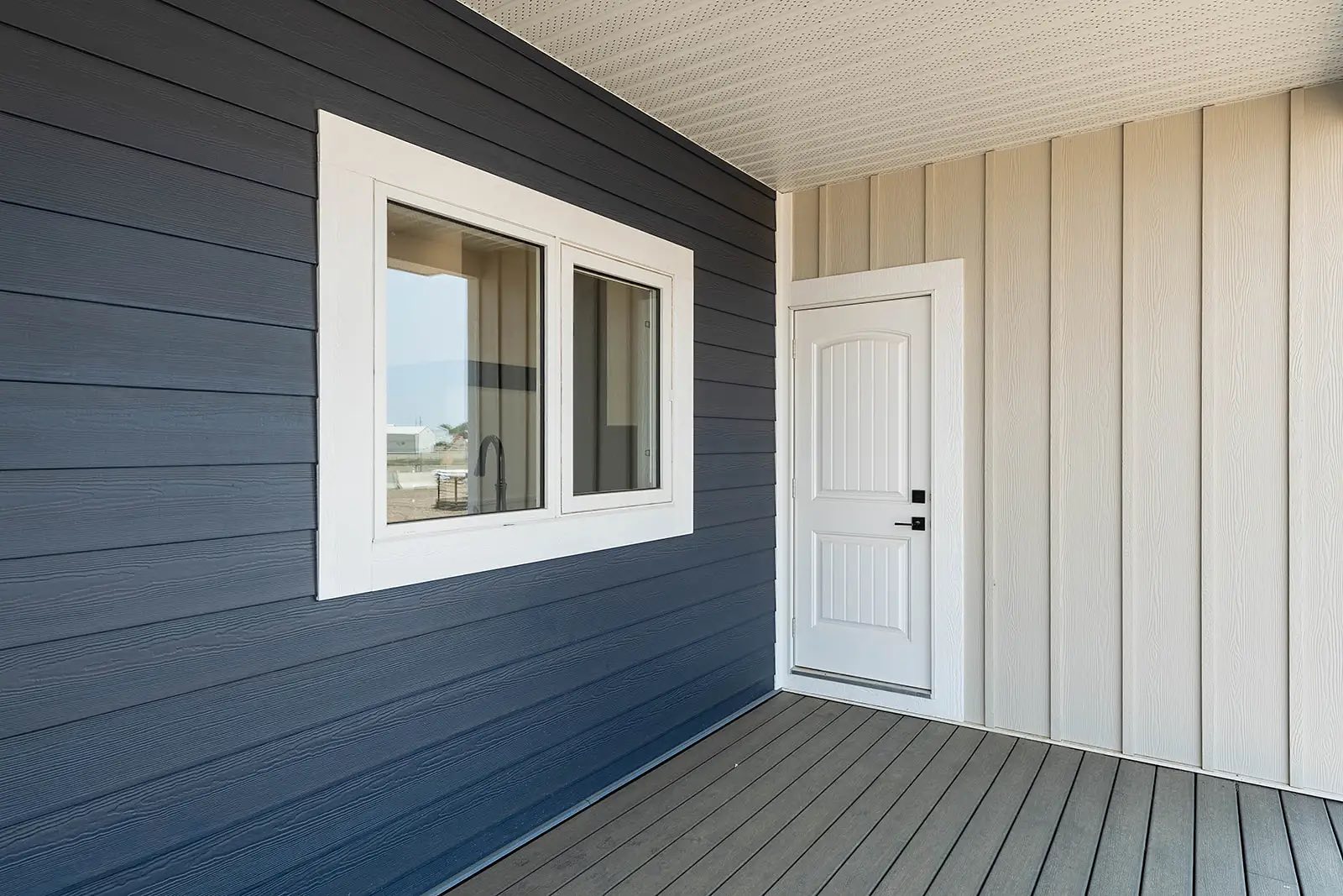 Modern porch with contrasting navy and beige siding, white-framed window, and a paneled door. Bright and clean atmosphere with a neat design.
