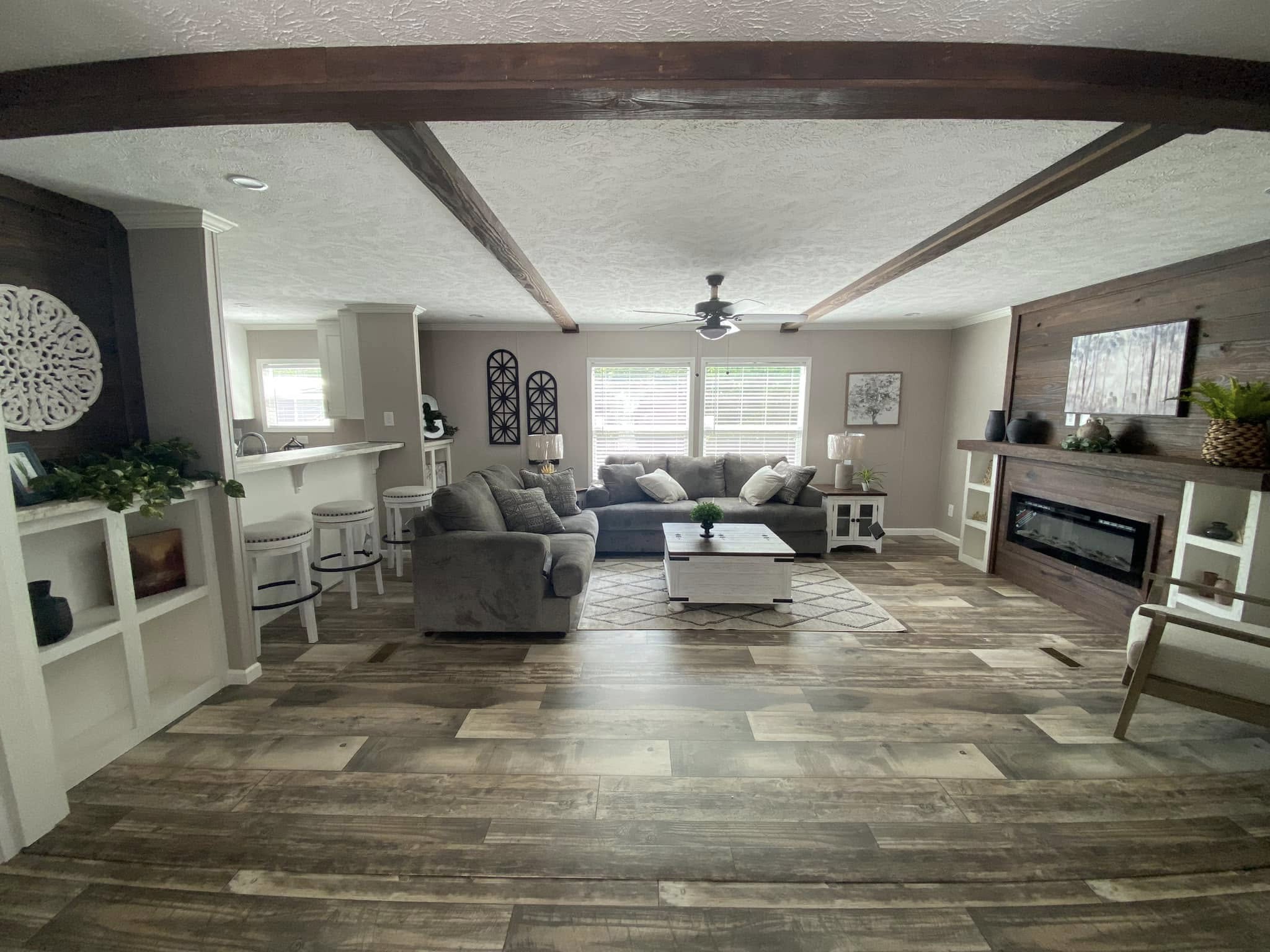 Stylish living room with wood flooring, gray sofa, and modern fireplace. Bright natural light, ceiling fan, and artwork create a cozy atmosphere.