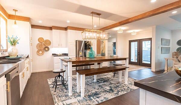 Modern kitchen with a central island featuring a wooden countertop, pendant lighting, and bar stools. Light walls and floor, with a decorative rug adding warmth.