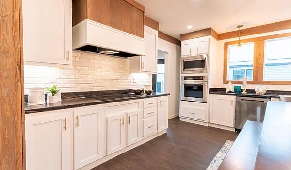 A modern kitchen with white cabinets, dark countertops, and stainless steel appliances. Warm lighting and wood accents create a cozy atmosphere.