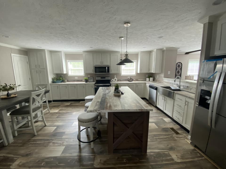 Spacious kitchen with wood floors, large island, bar stools, white cabinets, stainless steel appliances, and pendant lights. Bright, modern, and inviting.