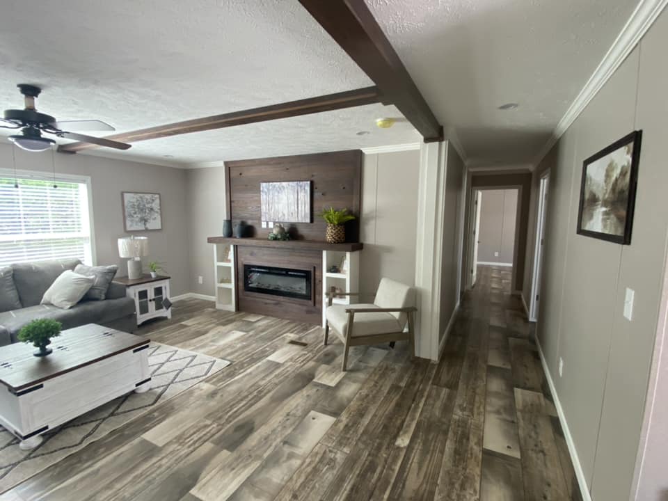 Stylish living room with wood flooring, gray sofa, and modern fireplace. Bright natural light, ceiling fan, and artwork create a cozy atmosphere.