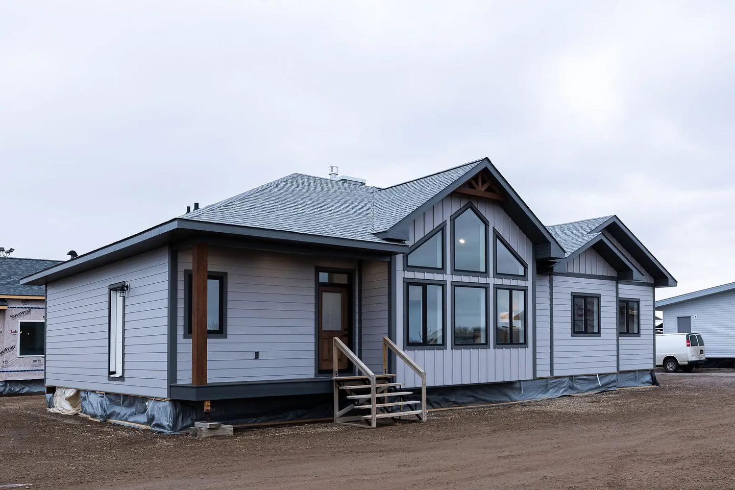 Modern modular home on a cloudy day, featuring large windows, gray siding, and a small entryway staircase, conveying a simple, inviting design.