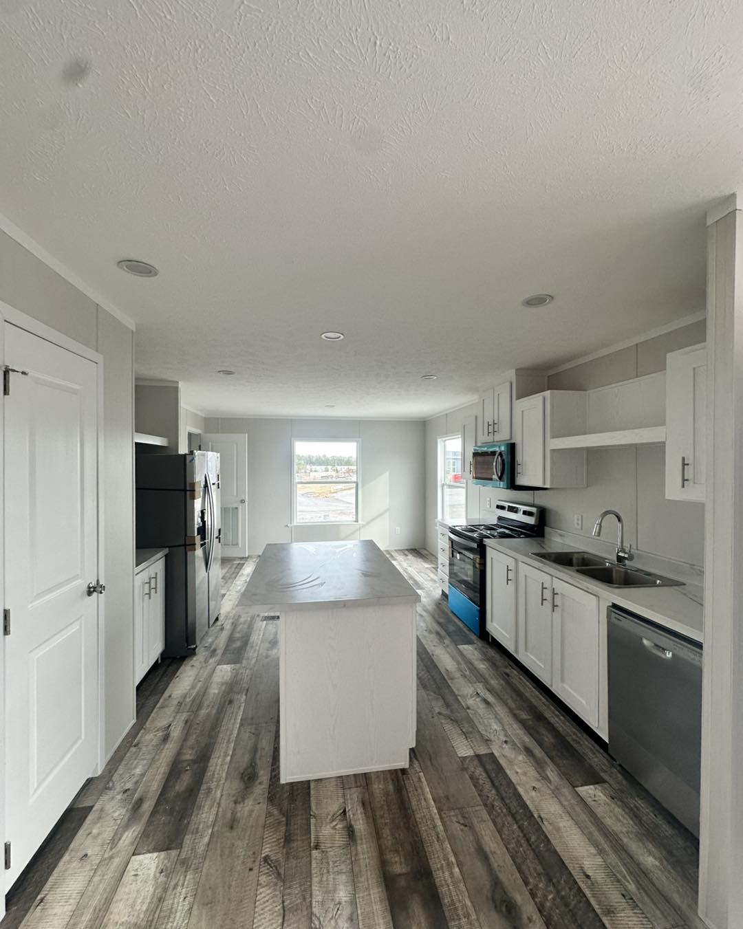 Modern kitchen with white cabinets, stainless steel appliances, and a center island. Sunlight streams through a window, highlighting wood floors.