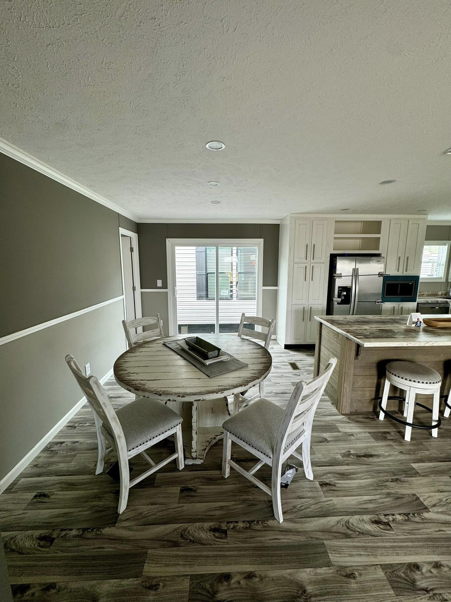 Cozy kitchen with a rustic round dining table and four chairs on wood flooring. A stylish island and stainless steel appliances enhance the modern feel.