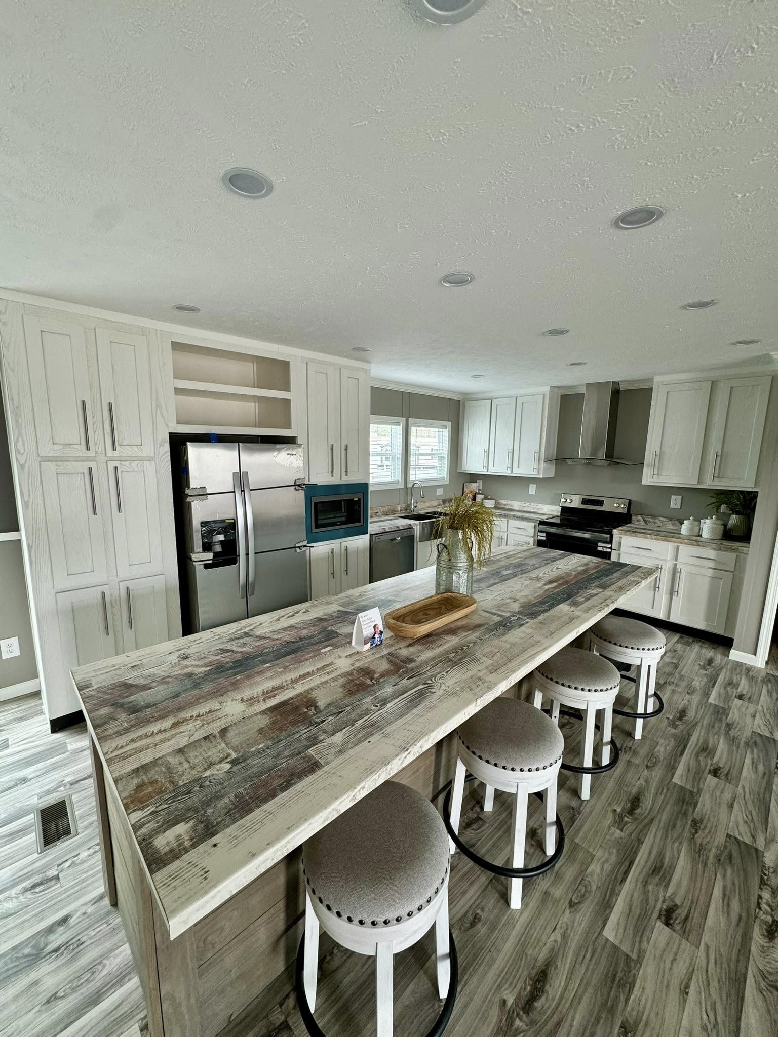 Spacious modern kitchen with rustic wood island, four cushioned stools, stainless steel appliances, and light gray cabinets. Bright, clean, welcoming.