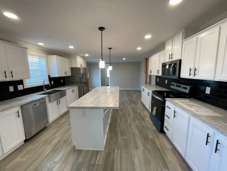 Modern kitchen with white cabinets, black backsplash, and stainless steel appliances. A long marble island and pendant lights create a bright, airy feel.