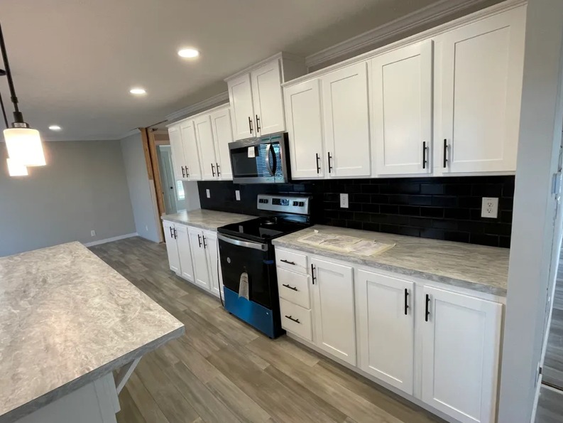 Modern kitchen with white cabinets, black subway tile backsplash, and gray countertops. Stainless steel appliances and pendant lighting create a sleek, clean look.