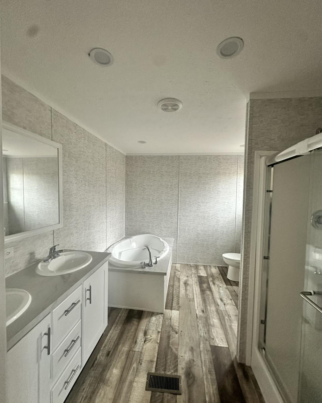 Empty room with light gray walls and wood-look flooring, featuring a large window allowing natural light. A bundle of baseboards lies on the floor. Minimalist tone.