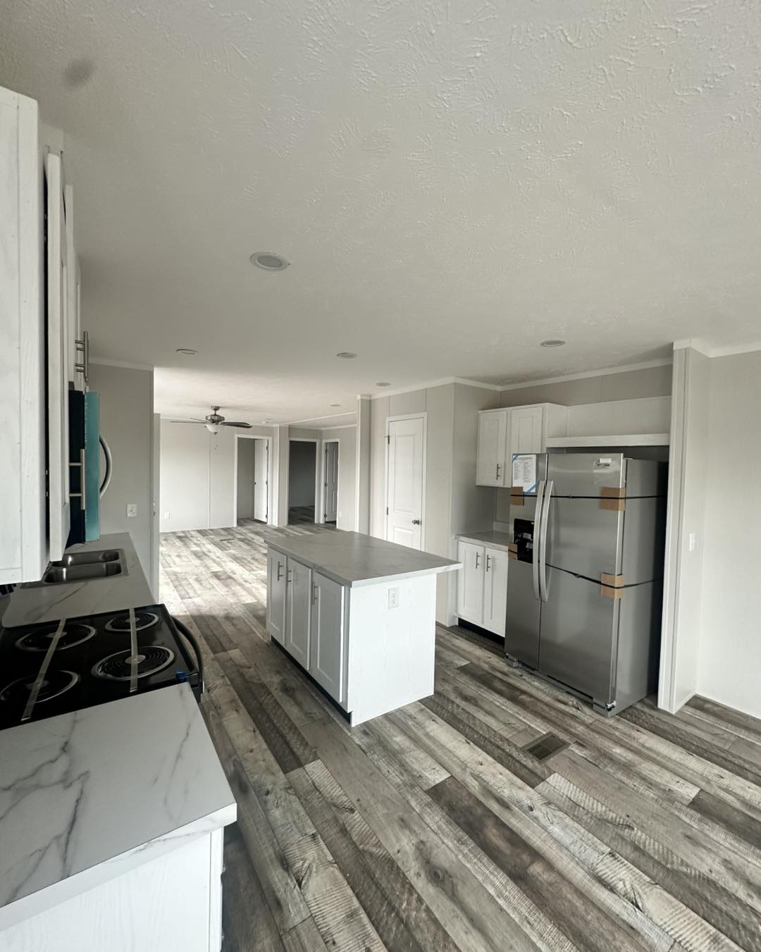 Modern kitchen with white cabinets, marble countertops, and stainless steel appliances. Features an island and wood-patterned vinyl flooring. Bright, open space with a calm, inviting ambiance.