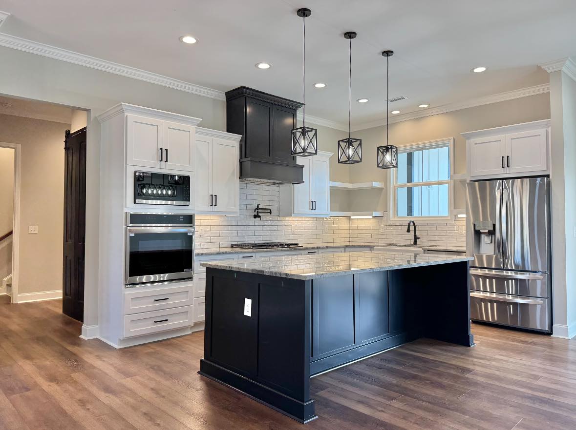 Modern kitchen with black and white cabinetry, marble island, stainless steel appliances, and pendant lights. Wooden floor adds warmth. Bright, sleek ambiance.