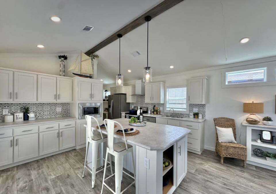 Spacious modern kitchen with white cabinets, island with two stools, stainless steel appliances, and decorative ceiling beams. Cozy and inviting ambiance.