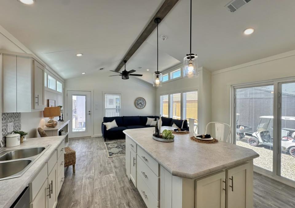 Bright, modern open-concept living area with a kitchen island, pendant lighting, and ceiling fan. Features a navy sofa, large windows, and cozy decor.