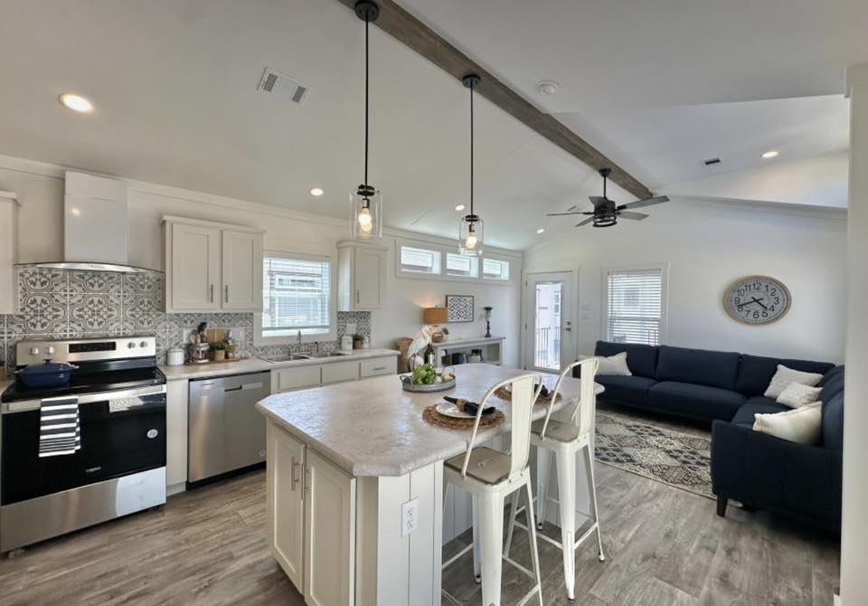 Spacious modern kitchen with white cabinets, island with two stools, stainless steel appliances, and decorative ceiling beams. Cozy and inviting ambiance.