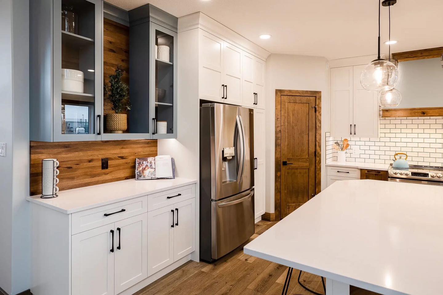 Modern kitchen with sleek white cabinets, stainless steel fridge, glass pendant lights, and wood accents. Warm, inviting ambiance with subway tiles.
