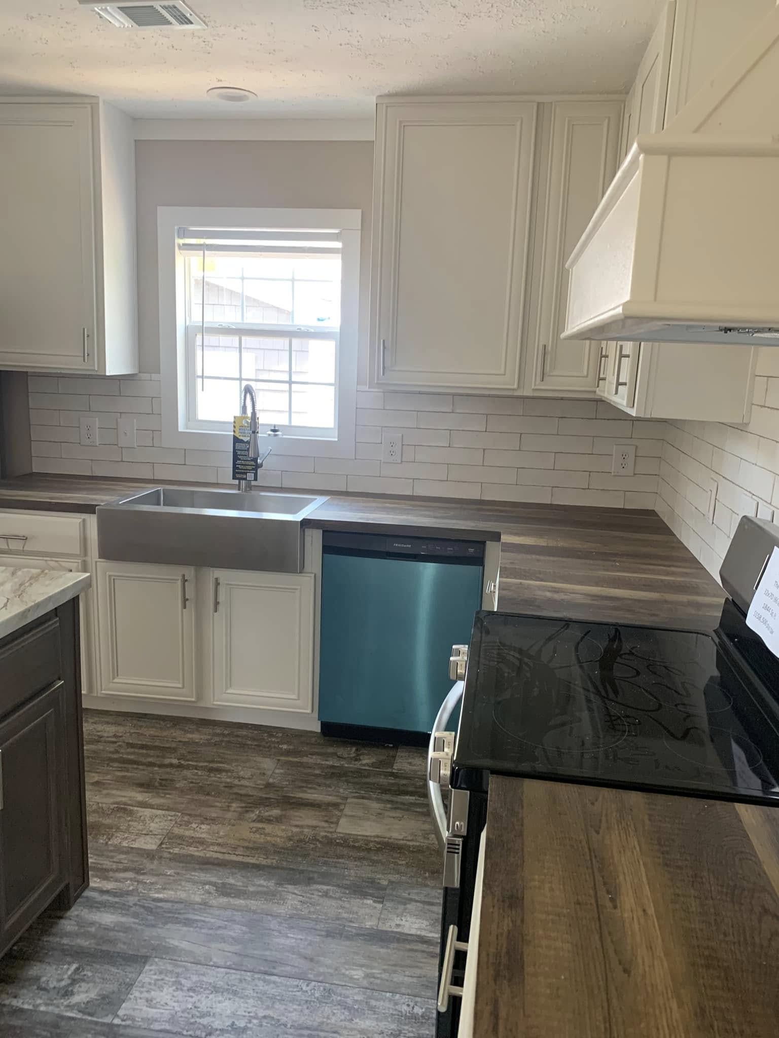 Modern kitchen with white cabinets, dark wood countertops, and a stainless steel farmhouse sink. A window provides natural light, creating a fresh and inviting atmosphere.