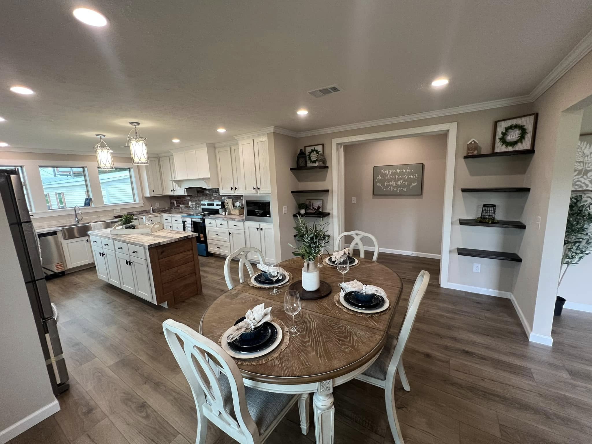 Modern kitchen and dining area with wooden floors, white cabinets, and recessed lighting. A round table is elegantly set for four, creating a cozy, welcoming atmosphere.