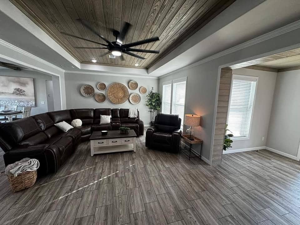 Warm, inviting living room with dark leather sofas, woven wall art, wood-plank ceiling, and soft lighting. Cozy and modern with earthy tones.