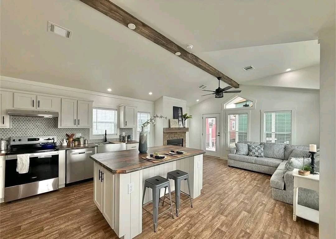 Spacious open-concept kitchen and living room with wooden floors, exposed beam ceiling, modern appliances, a center island, and a cozy gray sofa.