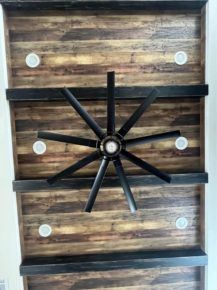 Wooden ceiling with a large black fan at the center, surrounded by four round white lights. The decor feels rustic and modern.