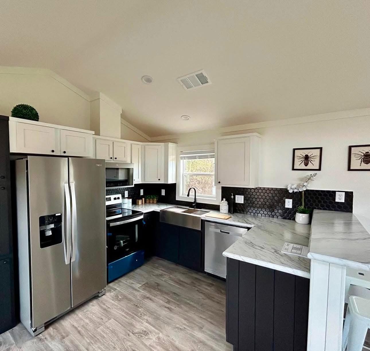 Modern kitchen with stainless steel appliances, white and dark cabinets, marble countertops, and hexagonal black tile backsplash. Bright and tidy.