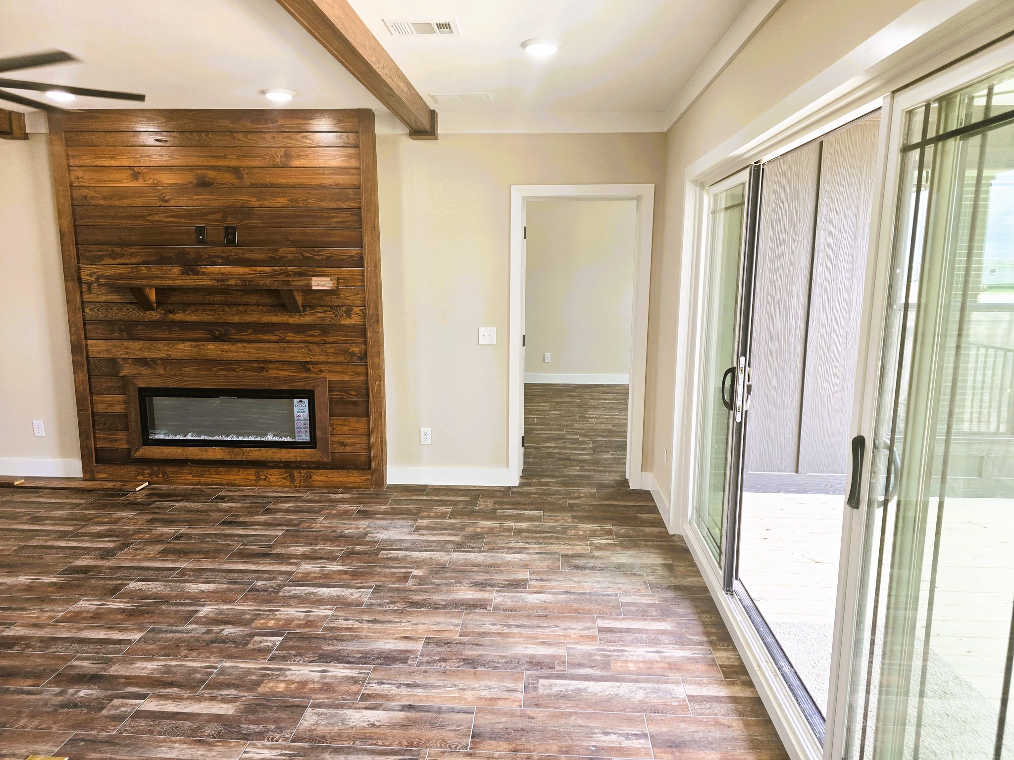 Spacious room with wood floors, a wooden accent wall featuring a built-in fireplace. Sliding glass doors open to a bright outdoor area. Cozy and inviting atmosphere.