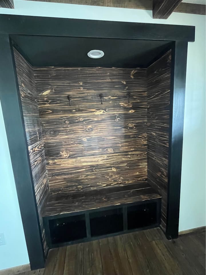 Dark wood nook with a bench, flanked by two coat hooks. The backdrop has a rustic, textured finish. The space has a cozy, inviting feel.
