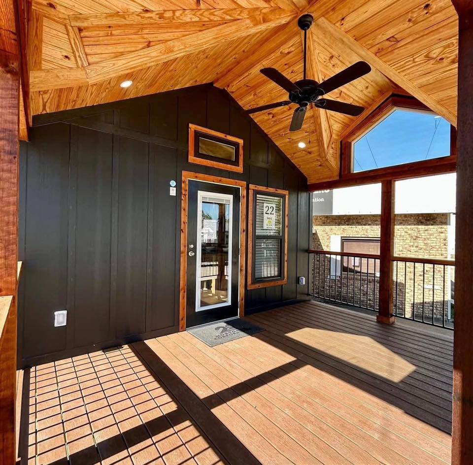 Warm, sunlit porch with a wooden vaulted ceiling, black fan, and glass door. Rustic charm with cozy atmosphere emphasized by natural wood.