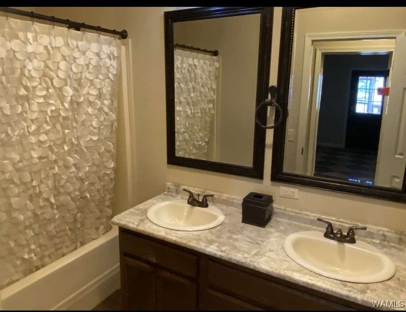 Bathroom features dual sinks on a beige marble countertop with dark wood cabinets. A ruffled white shower curtain and two large mirrors add elegance.