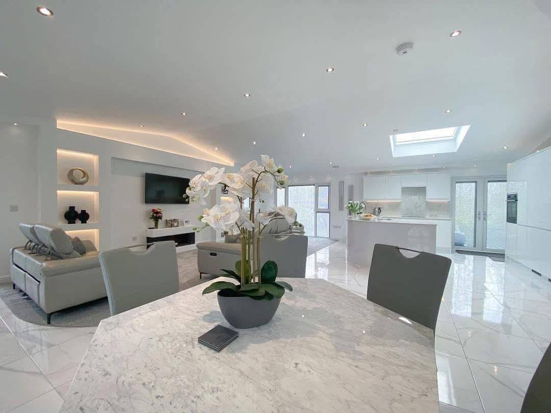 Spacious, modern living area with a marble table and white orchid centerpiece in the foreground. Open kitchen and cozy seating area, exuding elegance and tranquility.