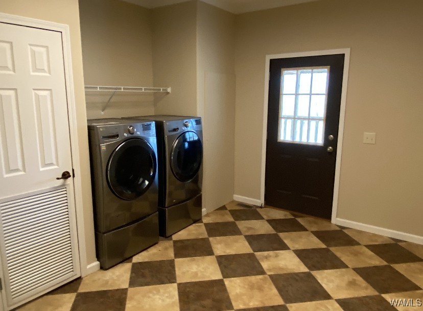 Laundry room with checkered tile floor, beige walls, and a dark door with a window. Features a silver washer and dryer set beside a white door.