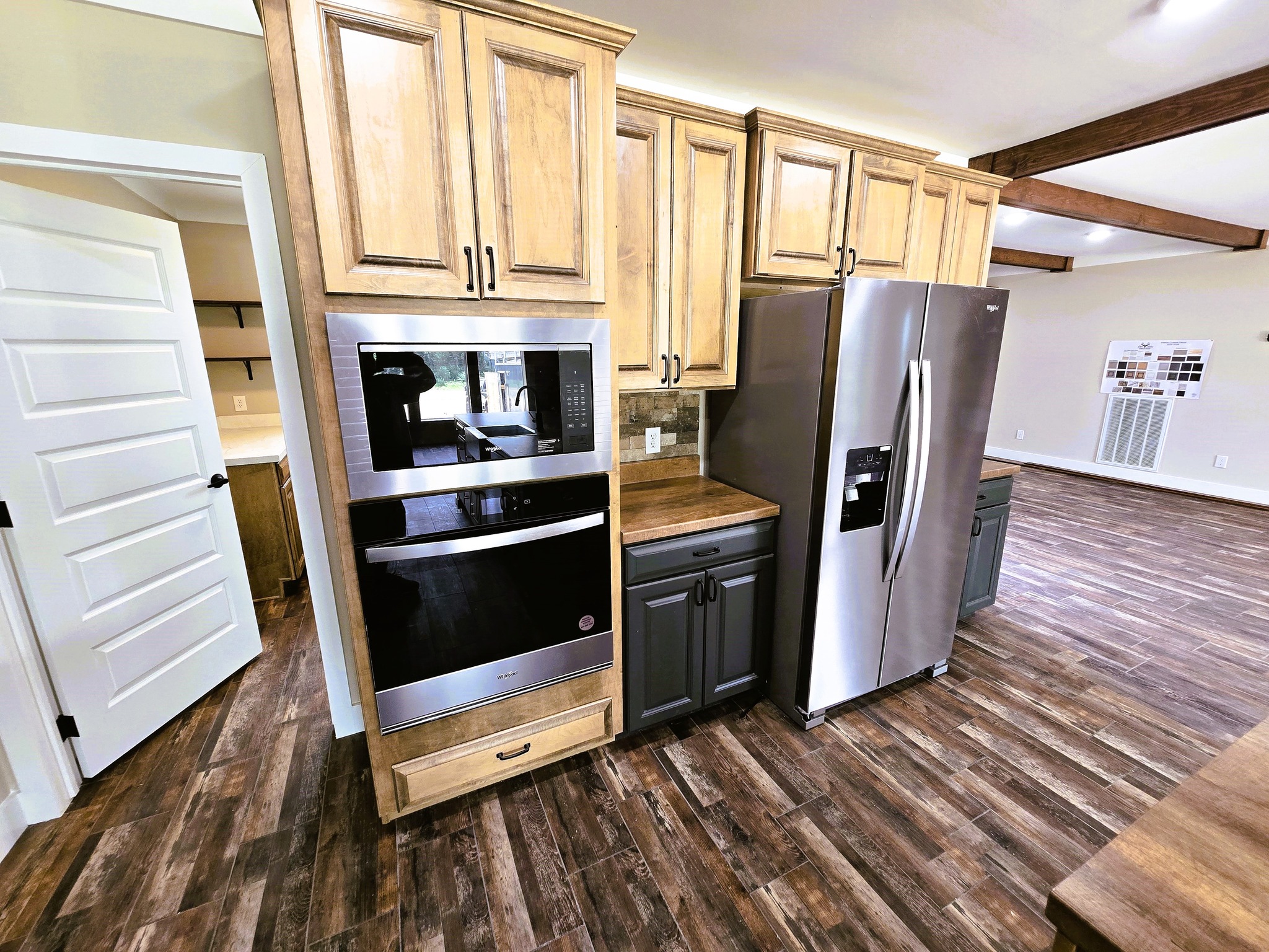 Modern kitchen with wood cabinetry, stainless steel fridge, built-in oven, and dark hardwood floors. The open plan has a warm, rustic feel.