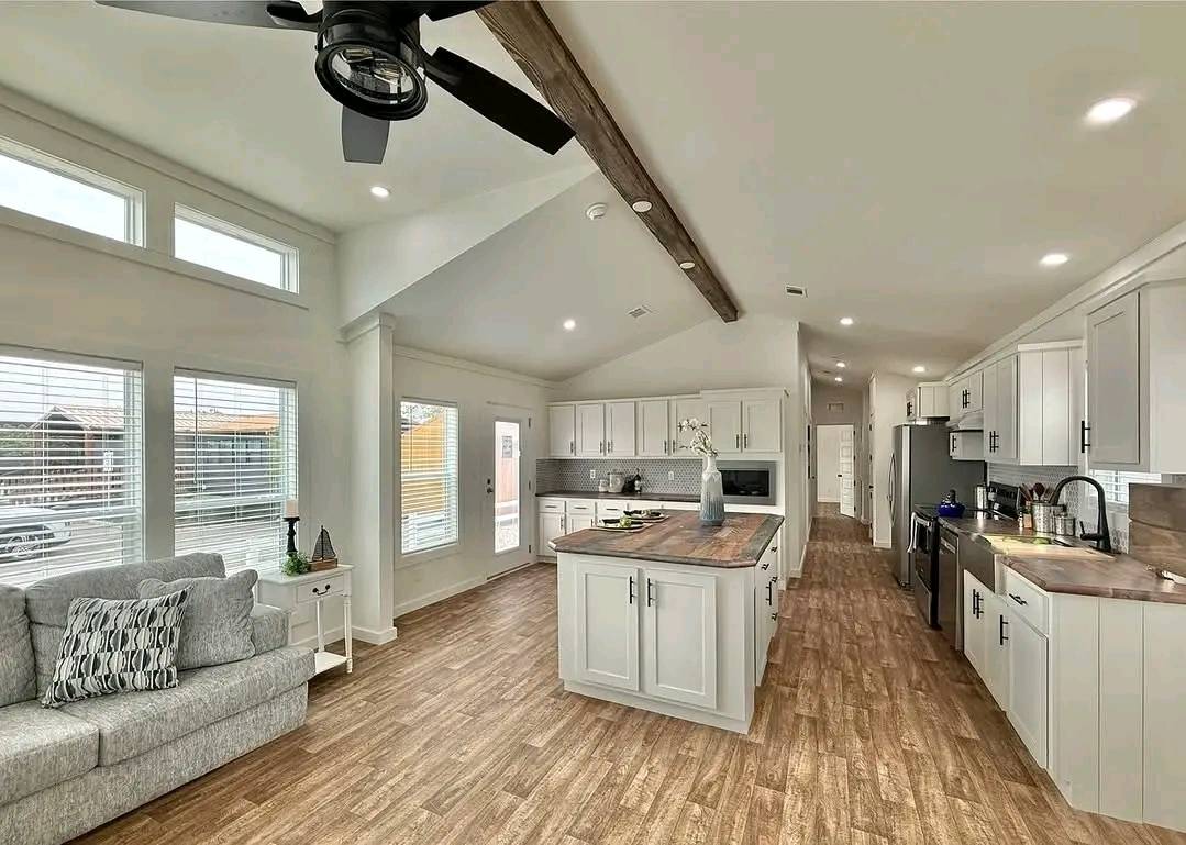 Modern kitchen and living area with wood floors, light gray cabinets, and a central island. Bright space with high ceilings and large windows. Cozy and inviting.